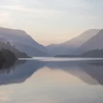 Lago en calma entre montañas con niebla